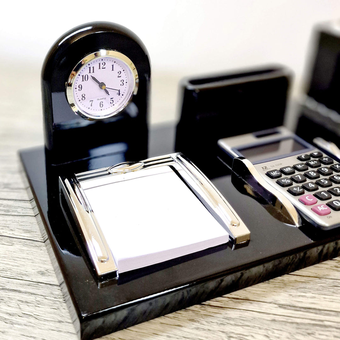 Black desk set with clock, calculator, and notepad on a wooden surface
