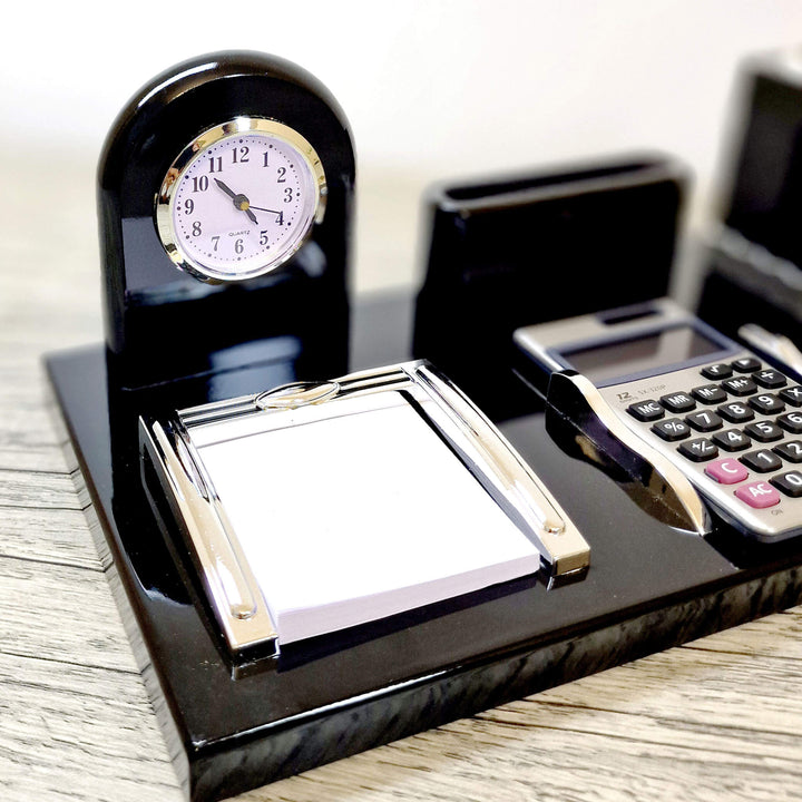 Black desk set with clock, calculator, and notepad on a wooden surface