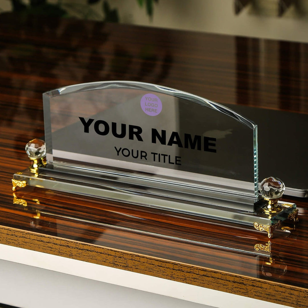 Clear glass nameplate with gold accents on a wooden surface